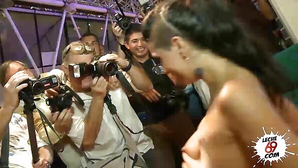 En blondin med ett sexigt leende täcker sin mun på en stor kuk på sängen